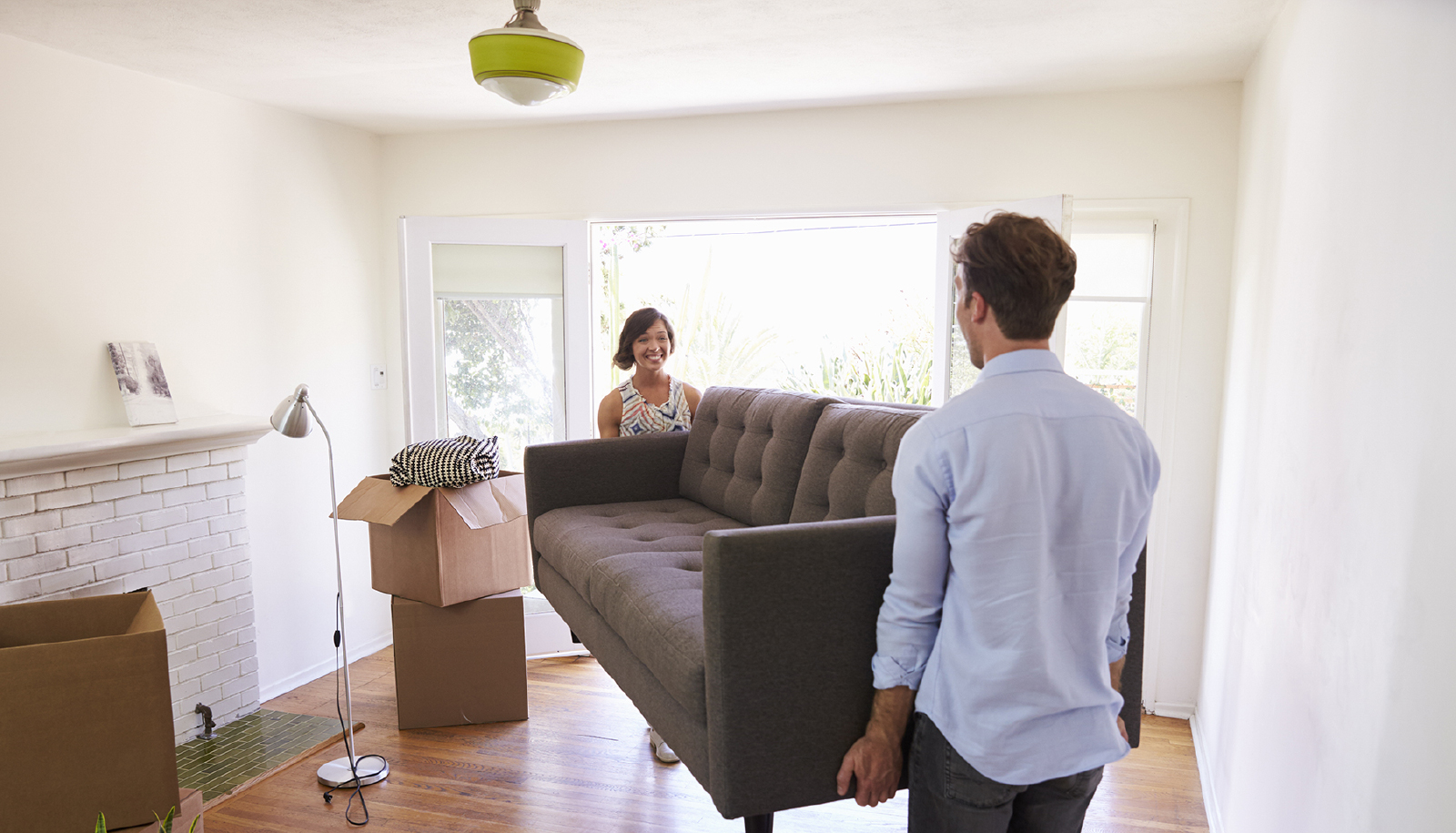 Two people carrying a brown sofa across the living room.